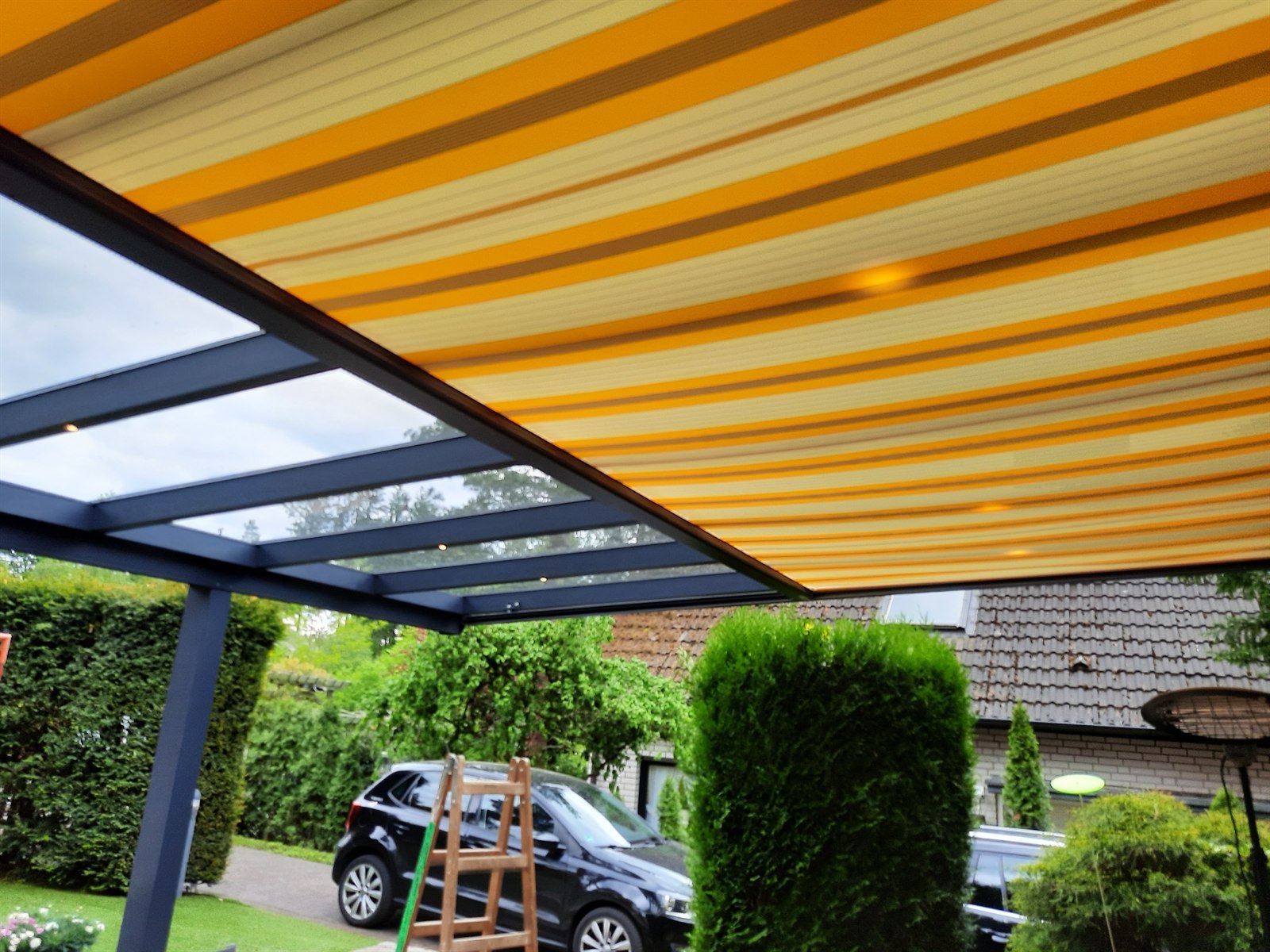 Ausgefahrene gelb gestreifte Dachbeschattung unter einem Aluminium-Terrassendach